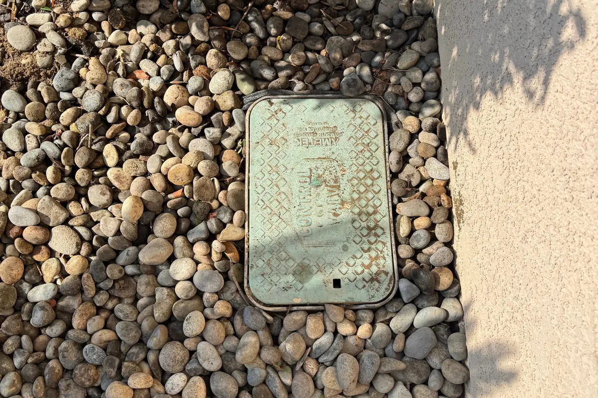 Sprinkler system irrigation valve box set in river rock beside a stucco wall in Bakersfield, CA
